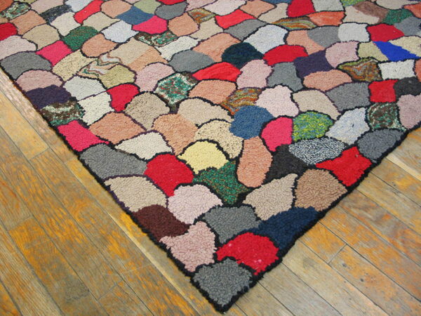 Close-up of a high-pile rug with irregular, multicolored patches on worn wood plank flooring.