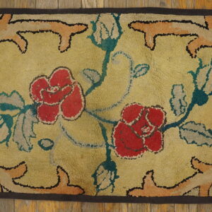A rectangular hooked rug featuring red roses on a yellow ground, framed by a dark border on wood flooring.