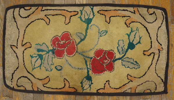 A rectangular hooked rug featuring red roses on a yellow ground, framed by a dark border on wood flooring.