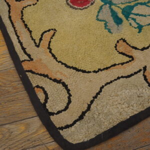 Textured loop rug corner with yellow, cream, and teal floral scrollwork resting on plank flooring.