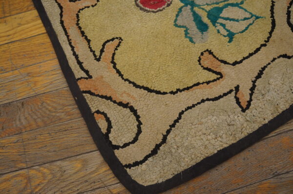 Textured loop rug corner with yellow, cream, and teal floral scrollwork resting on plank flooring.