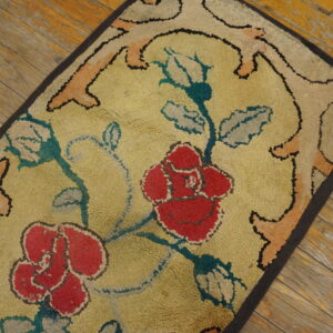 Textured rug with large red roses, teal stems, and a gold field on distressed plank wood flooring.