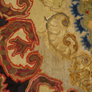 Looped pile rug detail in red, tan, and black on wood floor, featuring scrolling floral patterns.