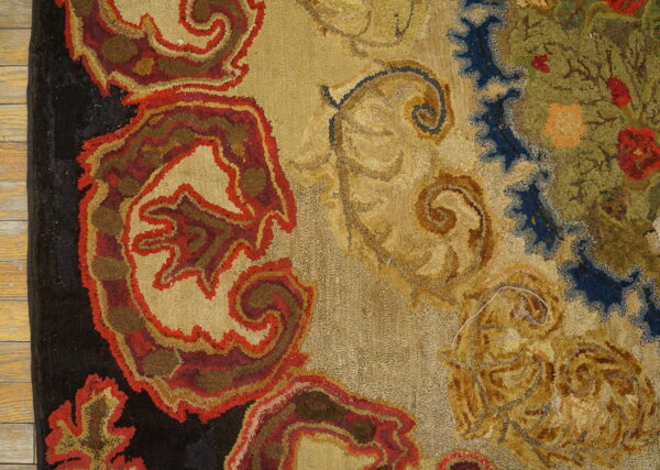 Looped pile rug detail in red, tan, and black on wood floor, featuring scrolling floral patterns.