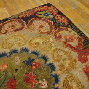 Multi-color hooked rug with red and gold scrolling border details displayed on light hardwood flooring.
