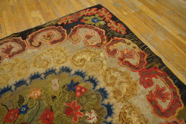 Multi-color hooked rug with red and gold scrolling border details displayed on light hardwood flooring.