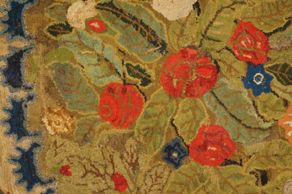 Rustic, textured rug detail showing red flowers, green foliage, brown vines, and a dark blue patterned border.