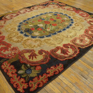 Textured rug with a floral medallion, deep red border, and gold field displayed on worn wooden plank flooring.