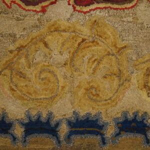 Highly textured rug detail features large golden ornamental scrolls and deep blue stylized border motifs.