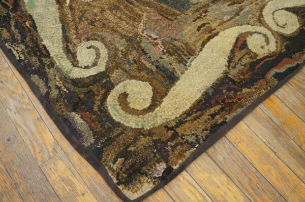 Textured rug corner showing cream scroll patterns and variegated browns on wide plank wood floor.