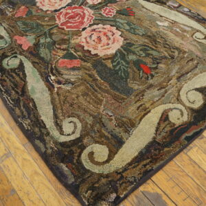 A hooked rug featuring pink roses, green leaves, and light scrolls rests on distressed wood plank flooring.