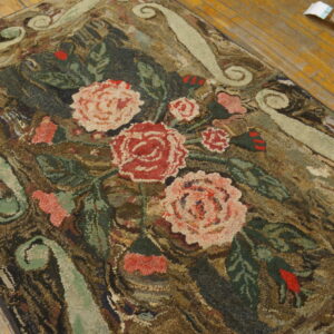 Coarse, floral hooked rug with pink and red roses on a dark ground over wood planks.