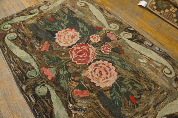 Coarse, floral hooked rug with pink and red roses on a dark ground over wood planks.