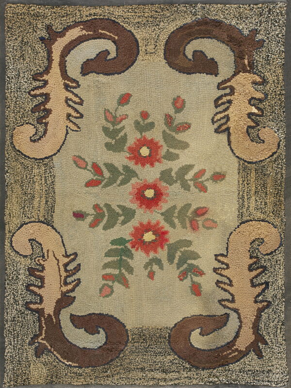 Textured rug with a floral center in red and green, framed by scrolling brown motifs and a dark speckled border.
