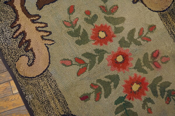 A highly textured rug with a sage green background, featuring red flowers and a tan scroll border.