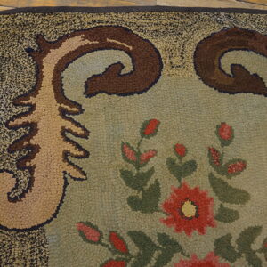 Textured loop pile rug featuring large red flowers, green vines, and scrolled brown corner designs on wood floor.