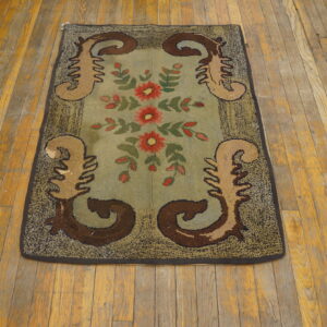 Hooked rug with red flowers and brown scrolls on a blue-green center, displayed on distressed wood floors.