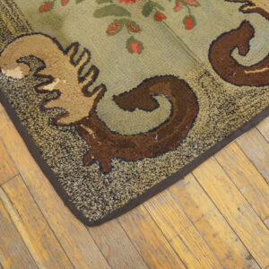 A looped green rug with scrolling brown and tan patterns sits on rustic, wide-plank wood floors.