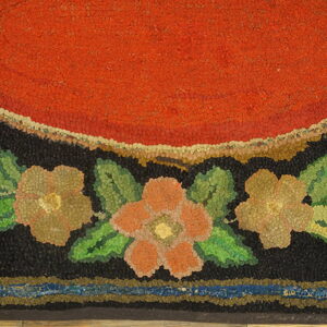 Hooked rug detail featuring a bright red center, black field, and a border of green leaves and multicolored flowers.