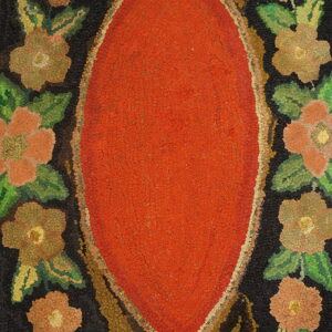 Close-up of a textured hooked rug with a reddish-orange oval center bordered by dark floral motifs.