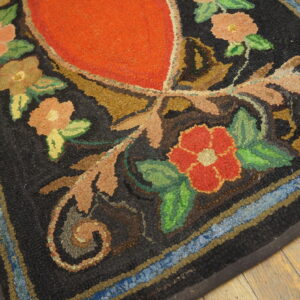 Hooked rug with a red center, multicolored floral patterns, black background, and striped border resting on wood planks.