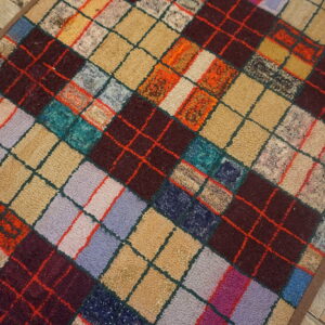 Textured, multicolored rug featuring a dense diamond argyle pattern on light, distressed wood plank flooring.