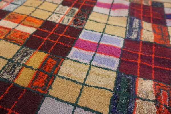 Multi-toned, looped pile rug featuring a vivid patchwork grid in shades of red, pink, beige, and blue.