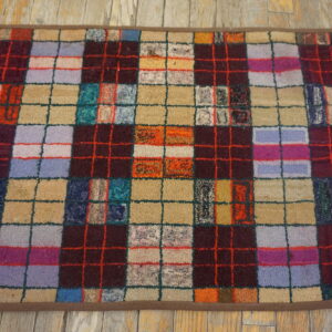 A nubby, multicolor checkerboard rug with dark vertical stripes rests on light distressed wood flooring.