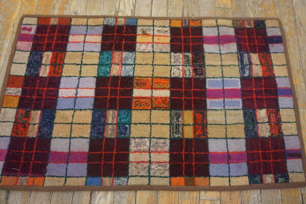 A nubby, multicolor checkerboard rug with dark vertical stripes rests on light distressed wood flooring.