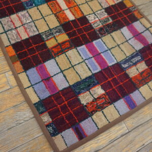A multicolored patchwork rug with a looped pile rests on distressed light wood floors.