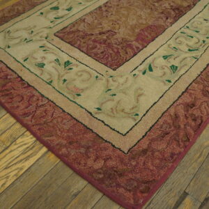 Textured maroon and beige area rug corner with green foliage pattern on worn wood plank flooring.