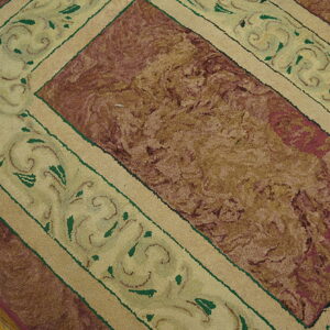 Textured rug featuring a burgundy and tan central field and a cream border with green scrollwork on wood floors.