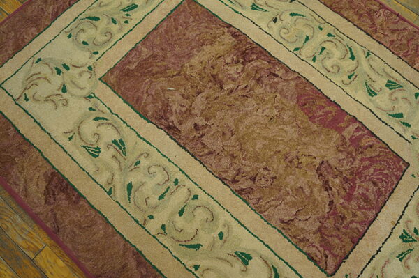 Textured rug featuring a burgundy and tan central field and a cream border with green scrollwork on wood floors.