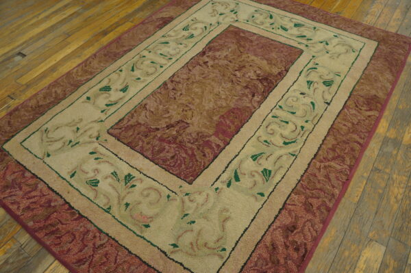 Beige and maroon rectangular rug with scroll borders resting on distressed wooden plank flooring.