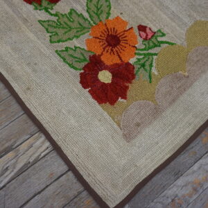 Textured beige rug featuring bright red and orange floral designs on weathered gray wood flooring.