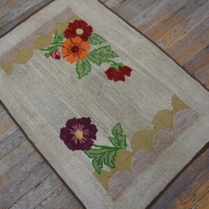 Beige textured rug featuring red, orange, and purple flowers rests upon rustic, weathered wood planks.