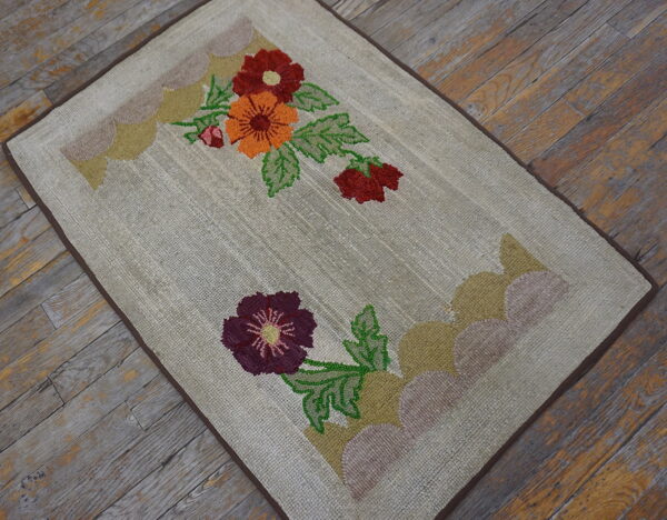 Beige textured rug featuring red, orange, and purple flowers rests upon rustic, weathered wood planks.