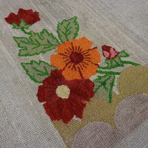 Close up of a beige looped rug featuring bright orange, red, and green stylized floral patterns.