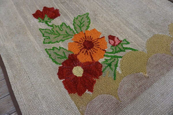 Close up of a beige looped rug featuring bright orange, red, and green stylized floral patterns.