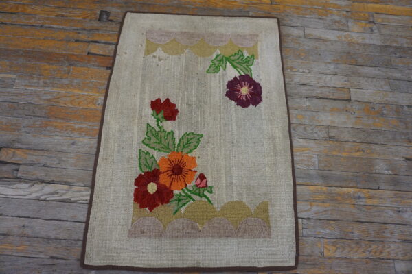 Beige loop pile rug featuring large red, orange, and purple flowers rests on a worn wooden floor.