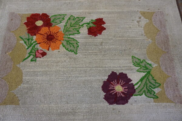 Looped rug featuring large orange, red, and purple flowers with a scalloped gold and pink border.