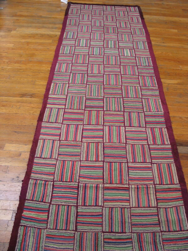 Multicolor striped patchwork runner with a maroon border lying on honey-toned wood planks.
