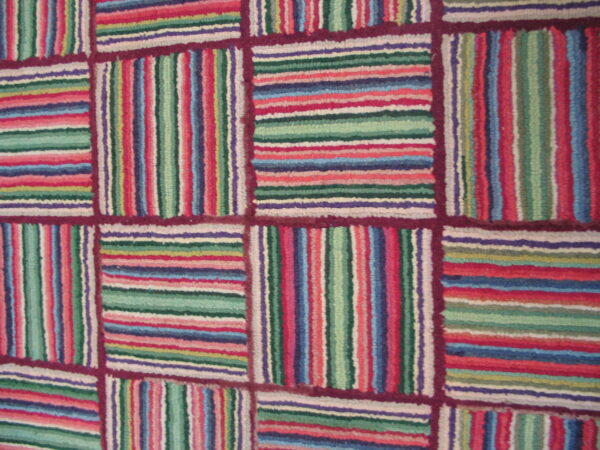 Textured rug with alternating blocks of colorful vertical and horizontal stripes framed by burgundy lines.