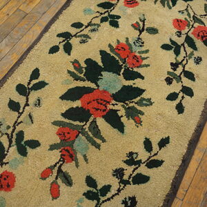 A textured tan runner rug displays red and green floral vines on distressed hardwood.