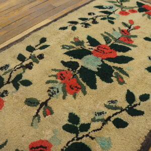 Beige loopy rug featuring red and green floral vines sits on a distressed wood floor.