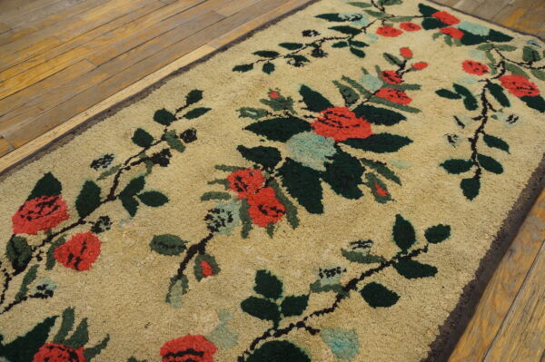 Beige loopy rug featuring red and green floral vines sits on a distressed wood floor.