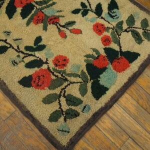 Looped tan rug featuring a red and dark green floral vine pattern rests on distressed wooden planks.