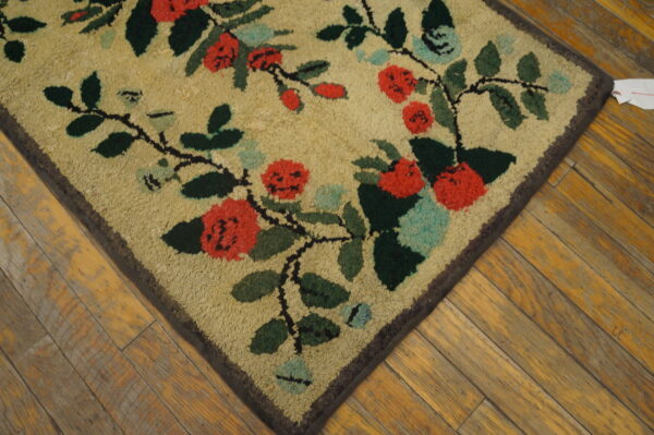 Looped tan rug featuring a red and dark green floral vine pattern rests on distressed wooden planks.