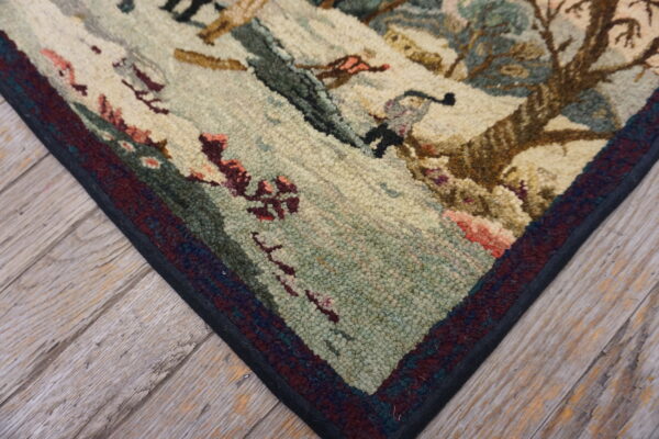 Textured corner of a pictorial rug with cream, sage, maroon, and brown colors resting on wood flooring.