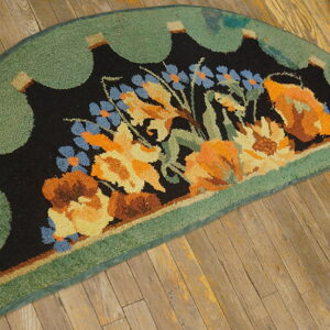Semicircular rug with black, orange, and blue floral pattern and a green scalloped border on rustic wooden floor.